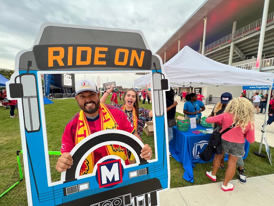 Man posing playfully with a "RIDE ON" photo prop of a MetroBus windshield as if he were the bus operator.